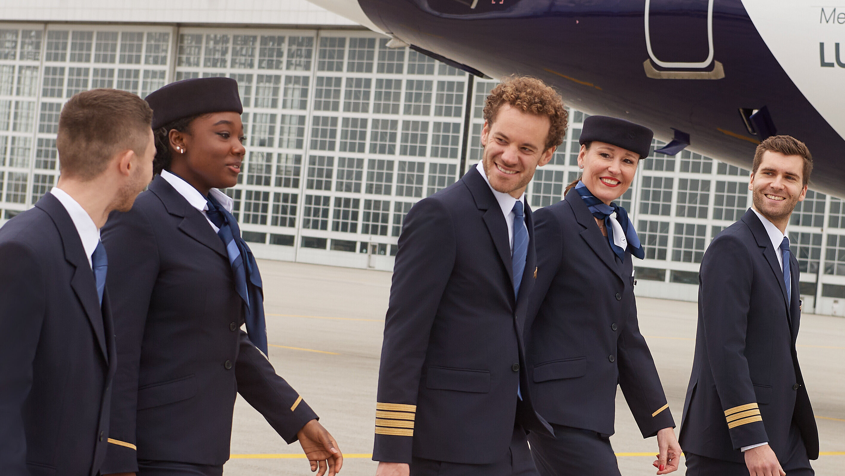 Fünf Lufthansa City Airlines Mitarbeitende, welche sich auf dem Vorfeld unterhalten, während sie ihr Gepäck mit sich führen